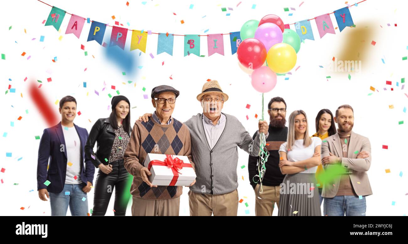 Senior friends with a present and balloons celebrating birthday with a group of young people isolated on white background Stock Photo