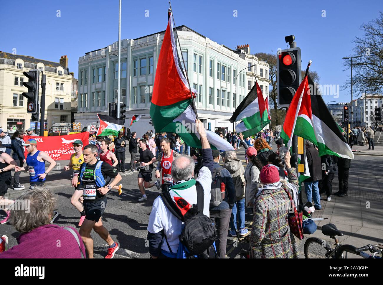 Brighton UK 7th April 2024 - Pro Palestine protesters wave flags as thousands of runners take part in the Brighton Marathon on a bright and sunny but windy day  : Credit Simon Dack / Alamy Live News Stock Photo