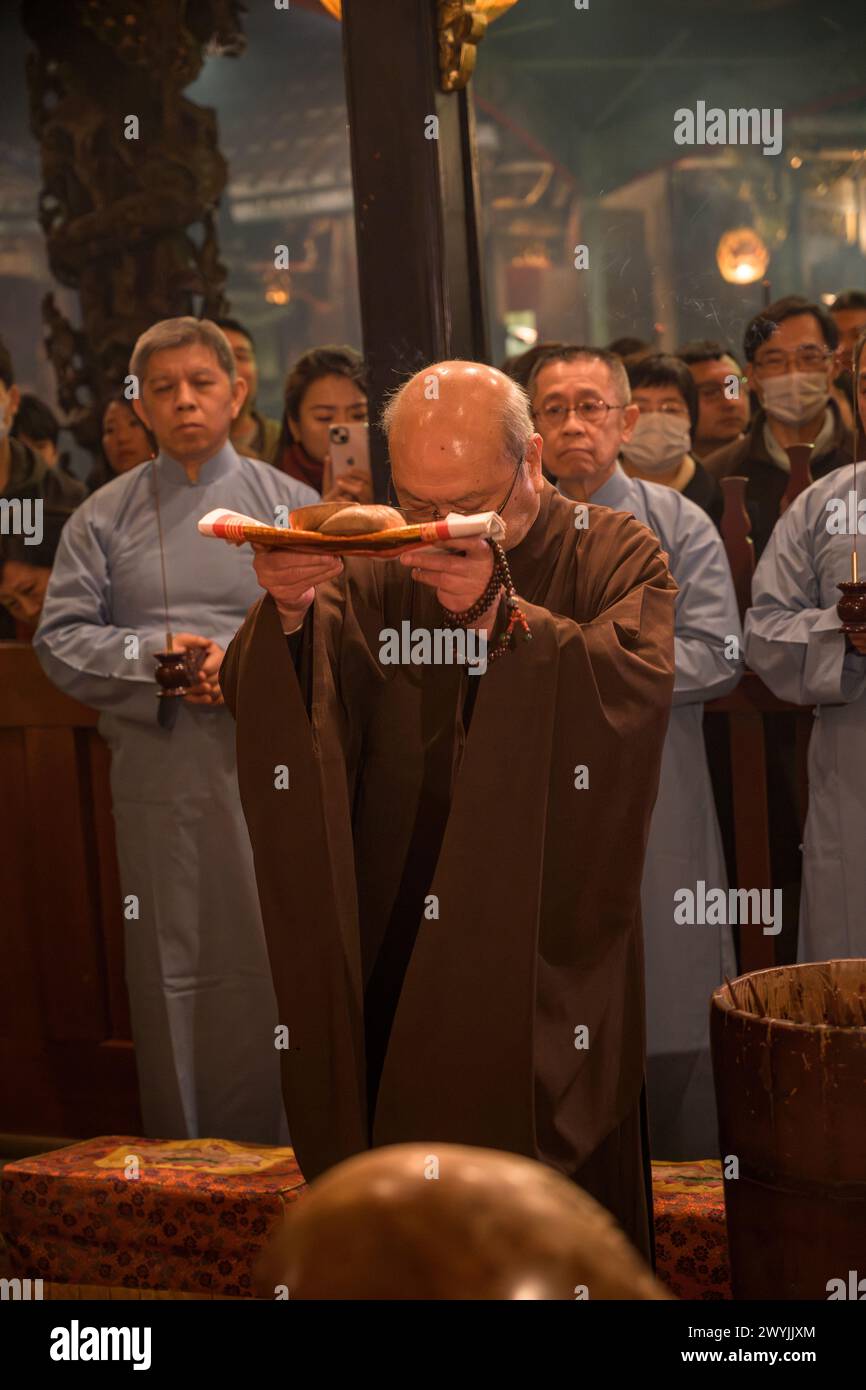 A monk deeply engrossed in prayer using prayer beads during a solemn religious Chinese New Year ceremony Stock Photo