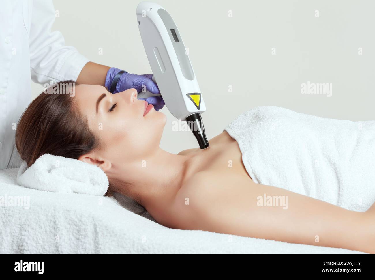 The cosmetologist is making carbon  peeling procedure on the collarbone and face in a beauty salon. Hardware cosmetology treatment. Stock Photo