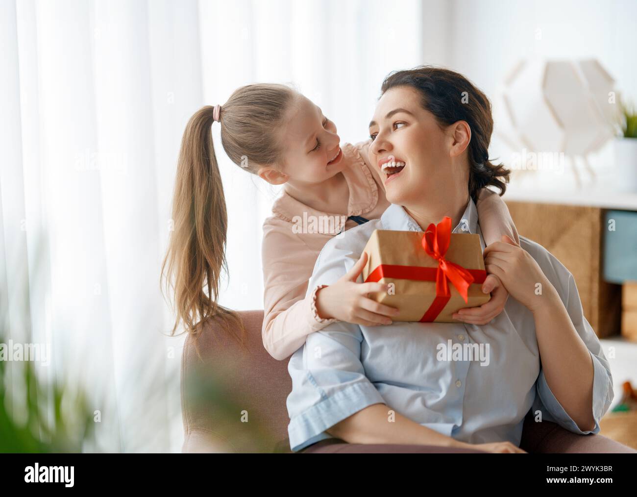 Happy mother's day. Child daughter is congratulating mom and giving her gift box. Mum and girl smiling and hugging. Family holiday and togetherness. Stock Photo