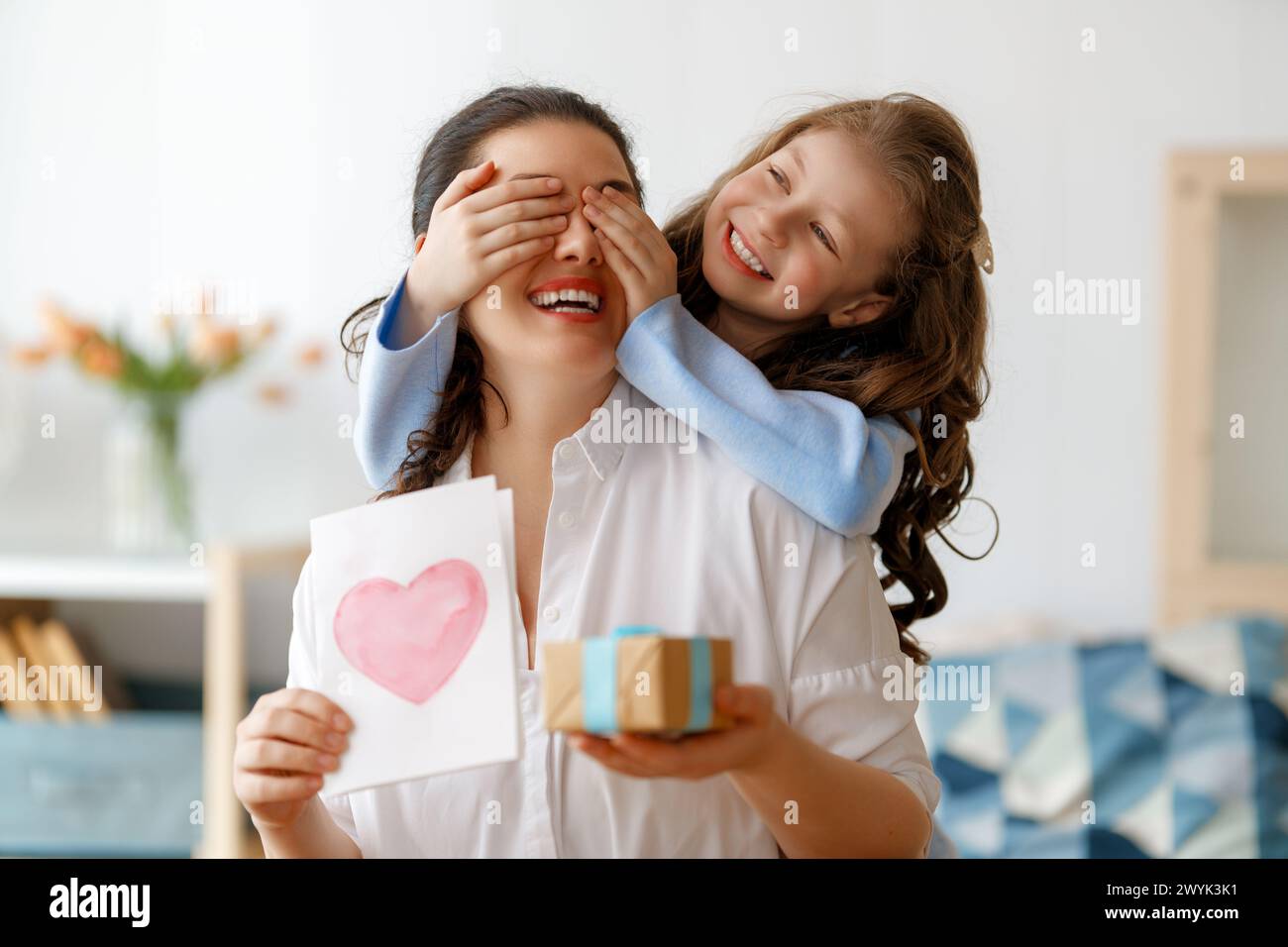 Happy mother's day. Child daughter is congratulating mom and giving her postcard. Mum and girl smiling and hugging. Family holiday and togetherness. Stock Photo