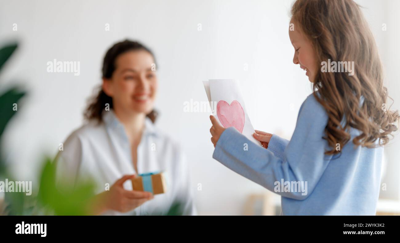 Happy mother's day. Child daughter is congratulating mom and giving her postcard. Mum and girl smiling. Family holiday and togetherness. Stock Photo