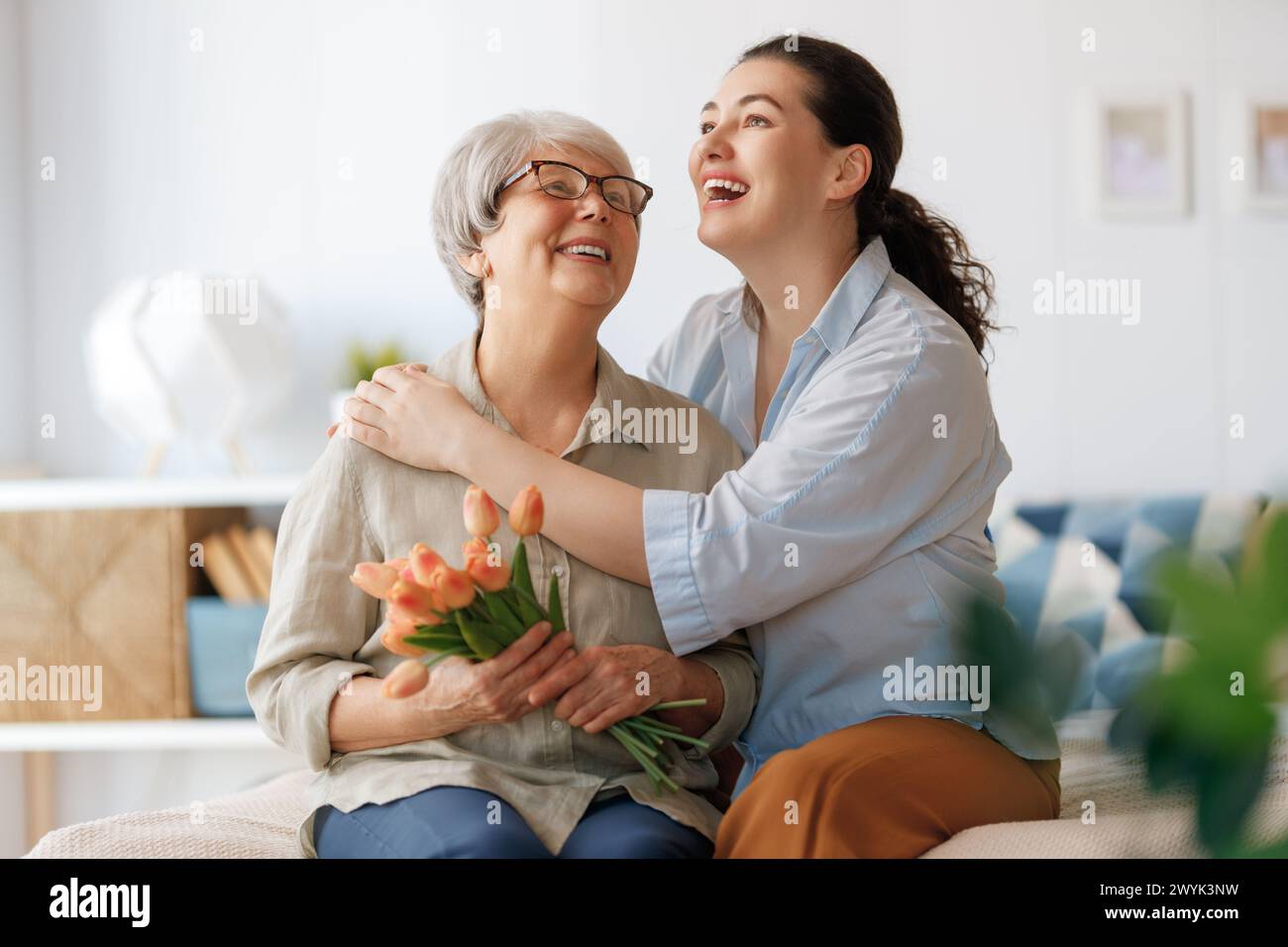 Beautiful young woman and her mother with flowers tulips in hands at home. Stock Photo