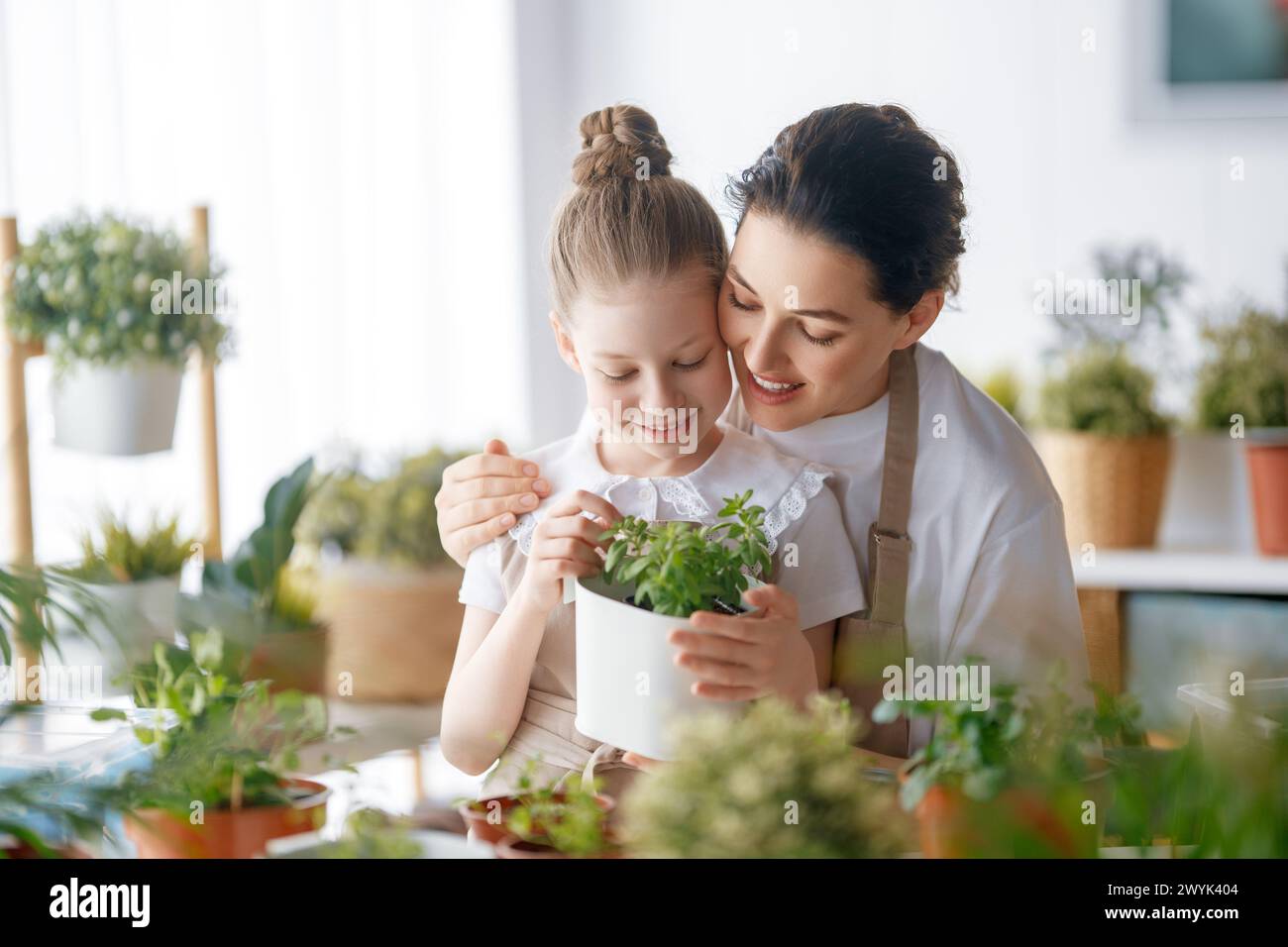 Cute child girl helping her mother to care for plants. Mom and her daughter engaging in gardening at home. Happy family in spring day. Stock Photo