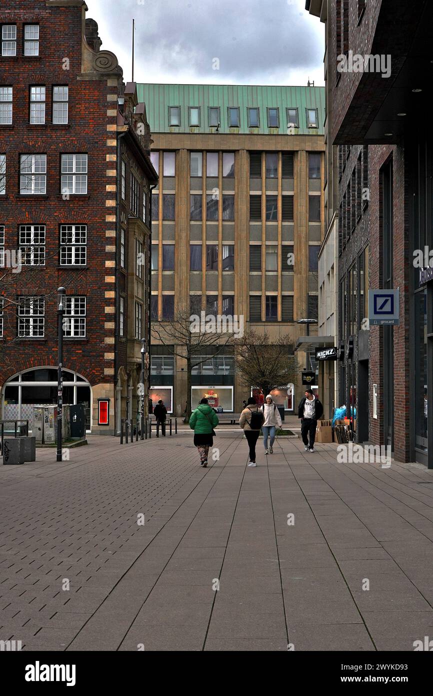 a portrait view of a street in Hamburg, with different colored buildings as people walk by on Easter Weekend, with Deutsche Bank logo on the side Stock Photo