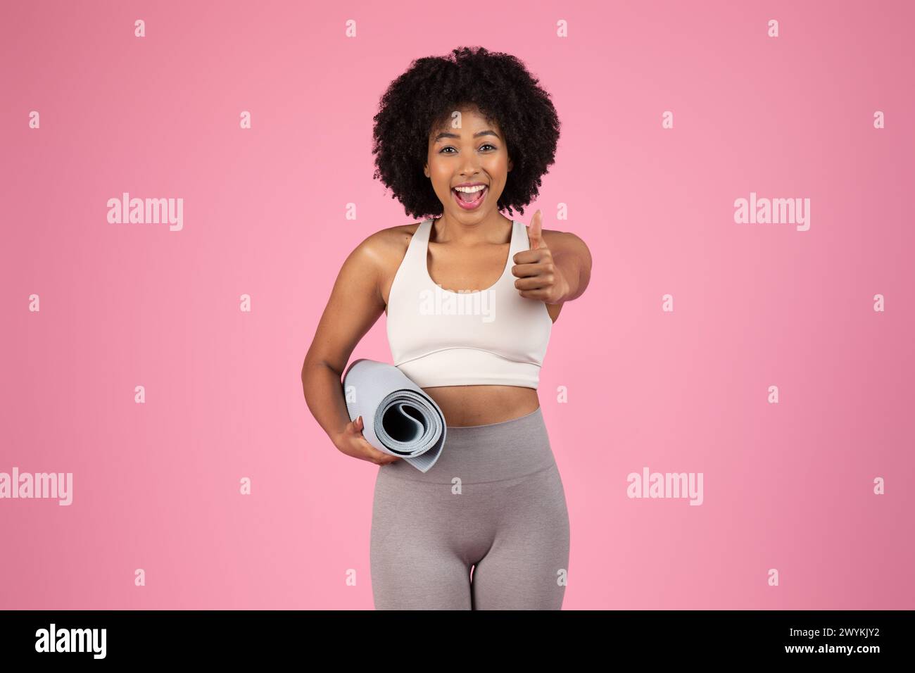 Happy woman giving thumbs up with yoga mat Stock Photo