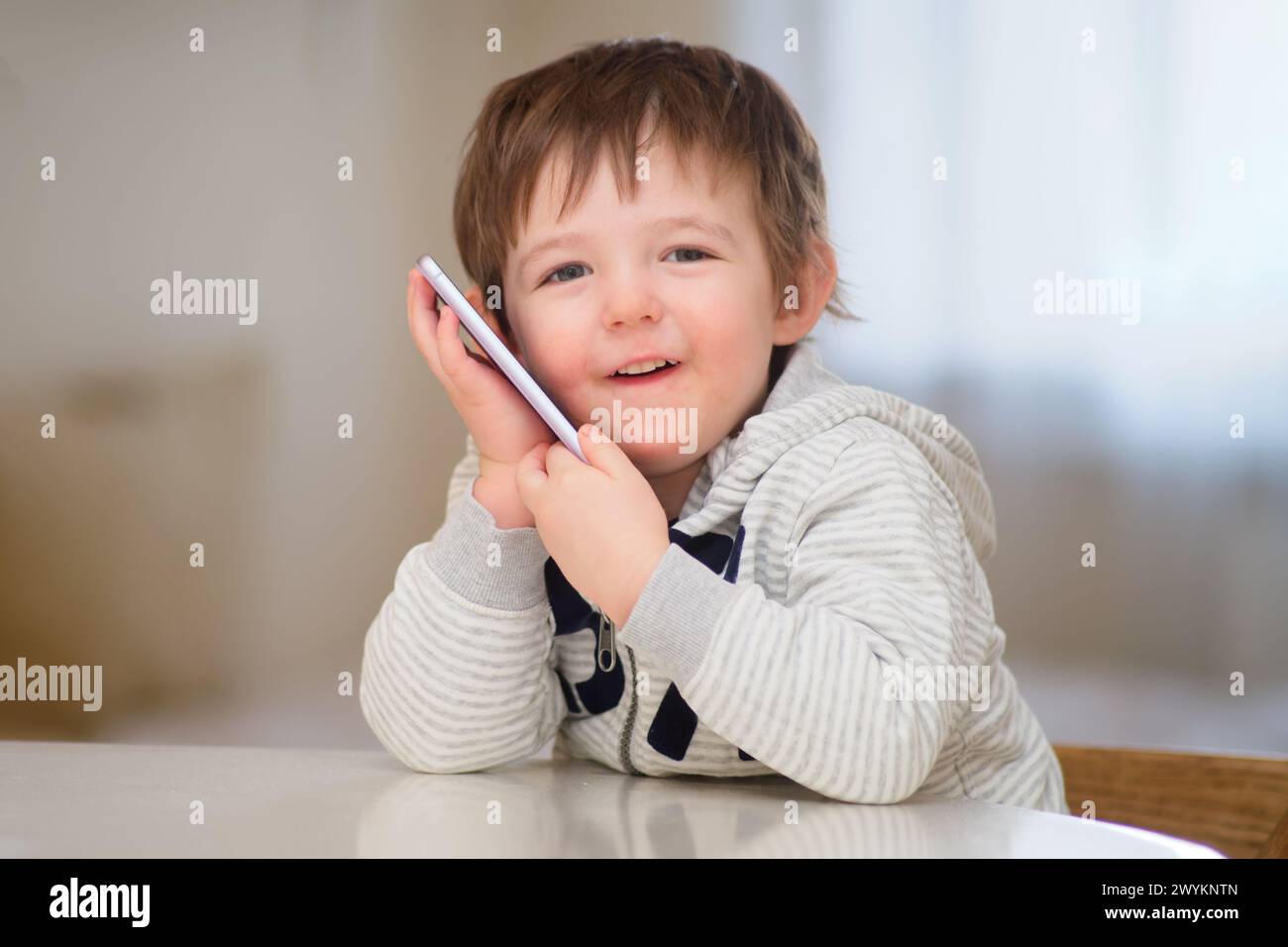 A happy baby is talking on a mobile phone. A smiling child is calling