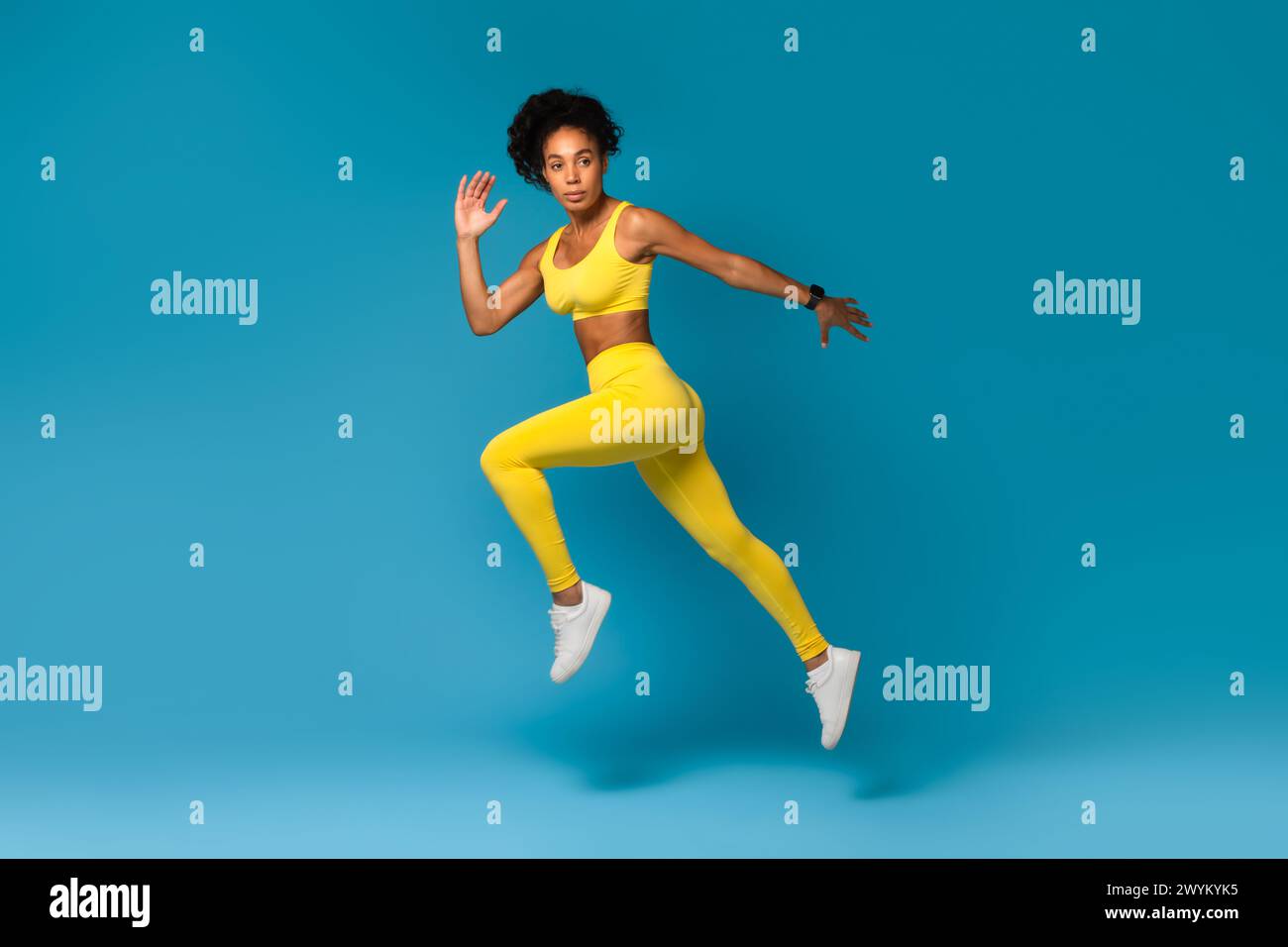 Athlete captured mid-air in yellow sportswear on blue background Stock Photo