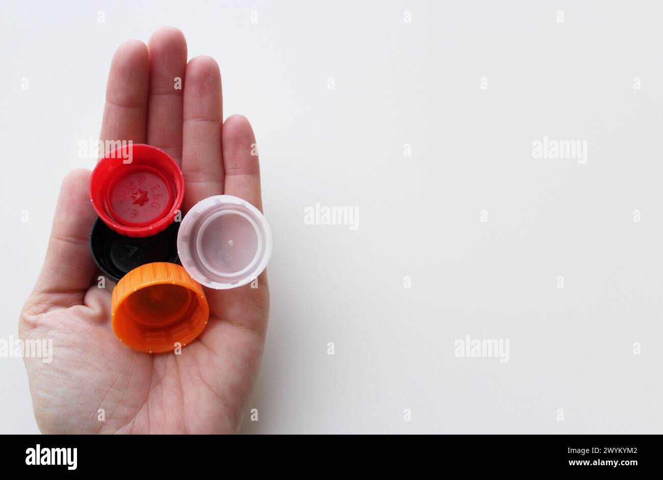 Woman's hand holding four plastic lids on white background, space for copy. Sustainability, recycling concept for June 5th World Environment Day Stock Photo
