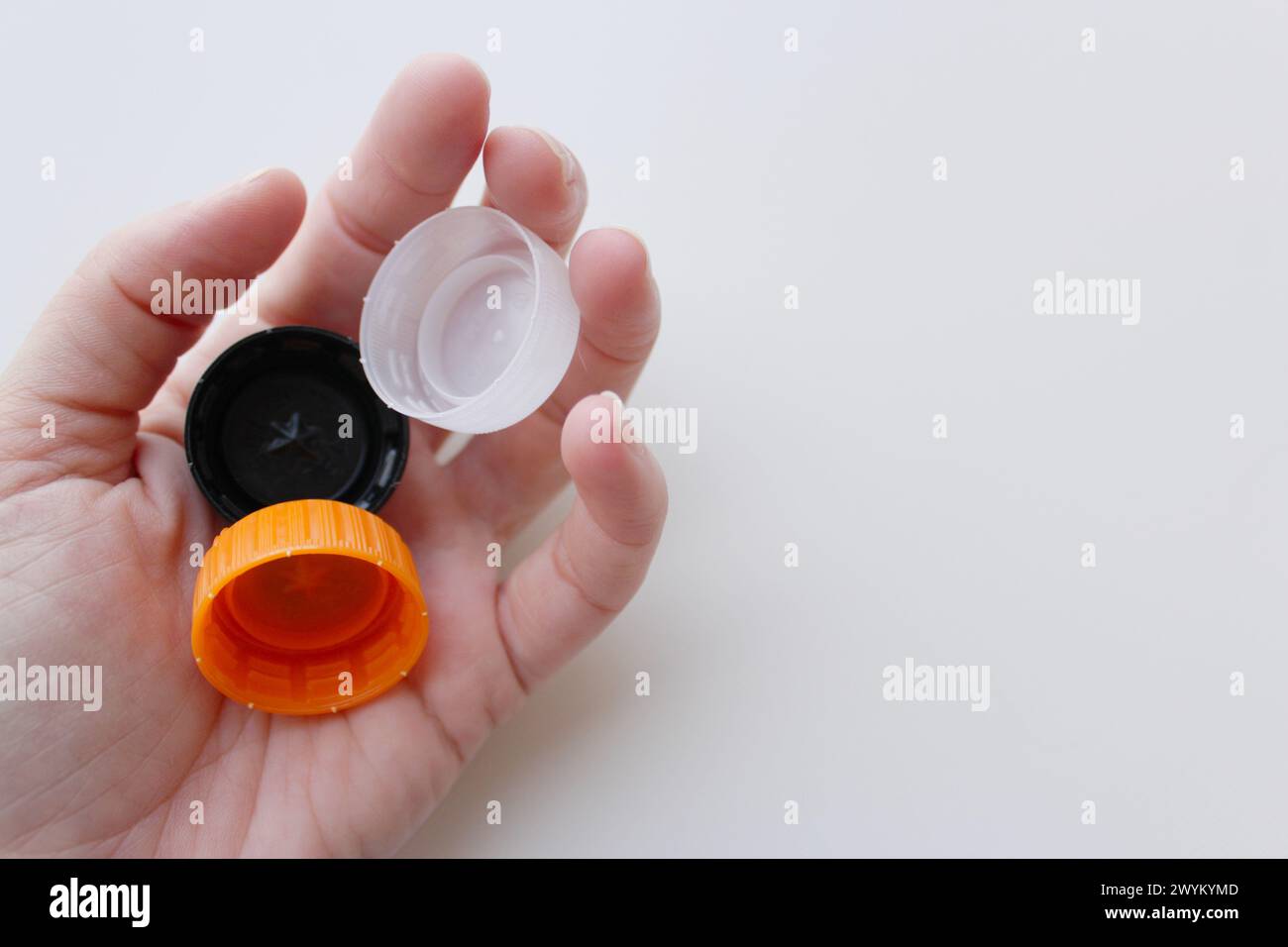 Woman's hand holding three plastic lids on white background, space for copy. Sustainability, recycling concept for June 5th World Environment Day Stock Photo