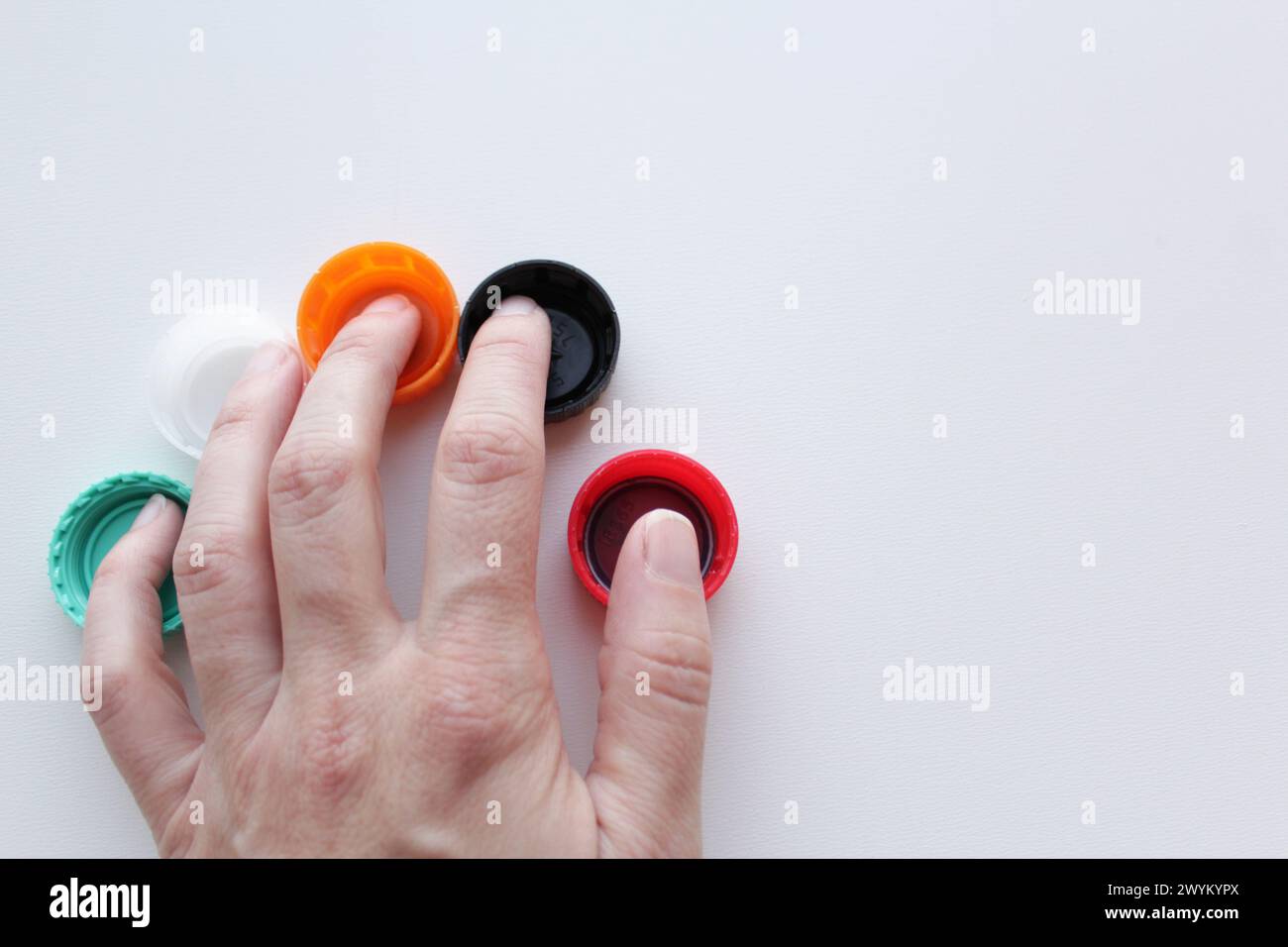 Woman's hand over five colorful plastic lids on white background, space for copy. Sustainability, recycling concept for June 5th World Environment Day Stock Photo
