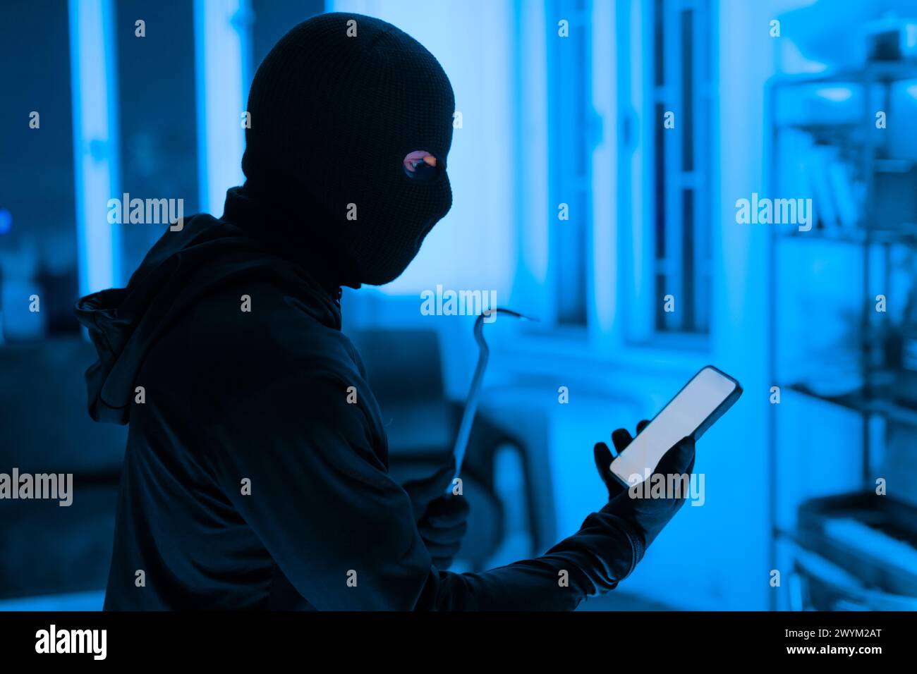 Thief using a smartphone during a break-in Stock Photo