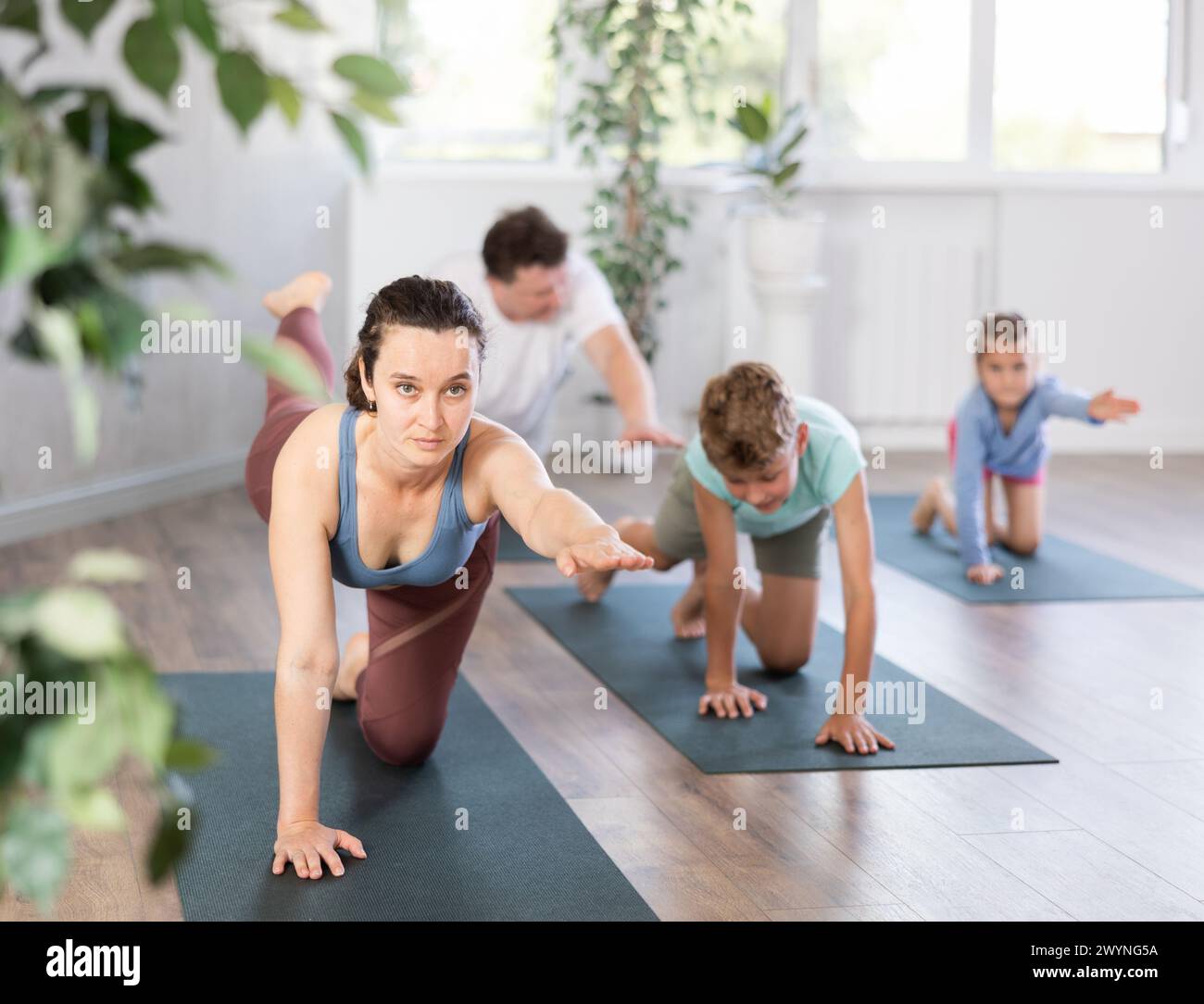 Willing middle-aged woman practicing table pose of yoga with her family ...