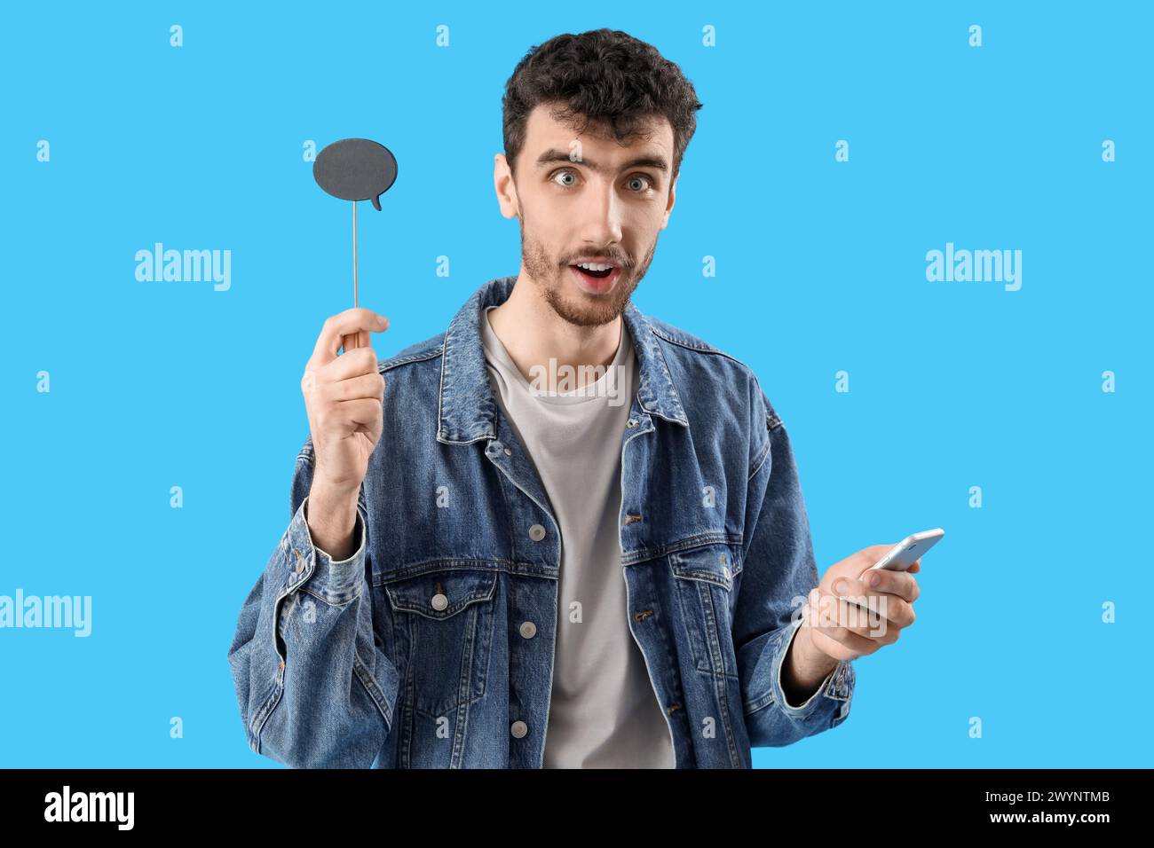 Surprised young man with speech bubble using mobile phone on blue background Stock Photo