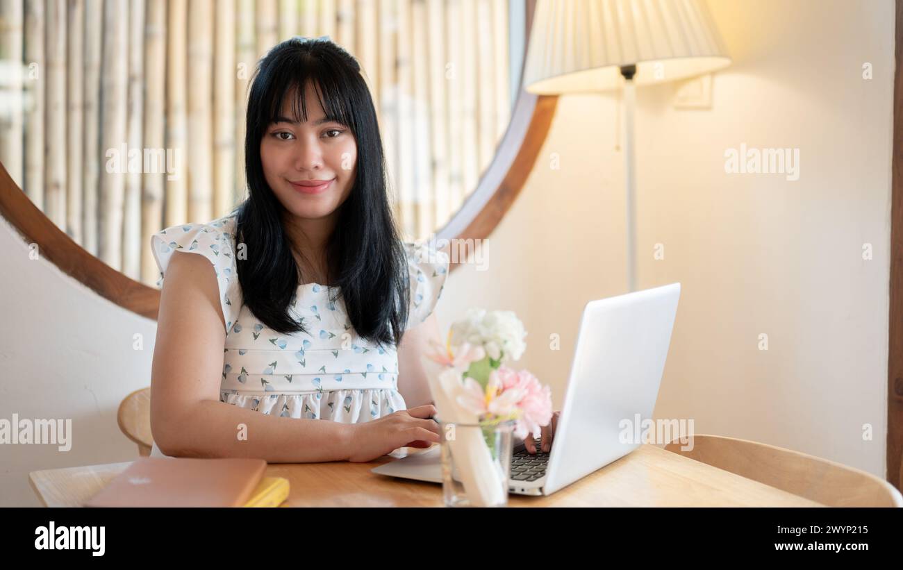 A cute young Asian woman in a cute dress sits at a table in a coffee ...