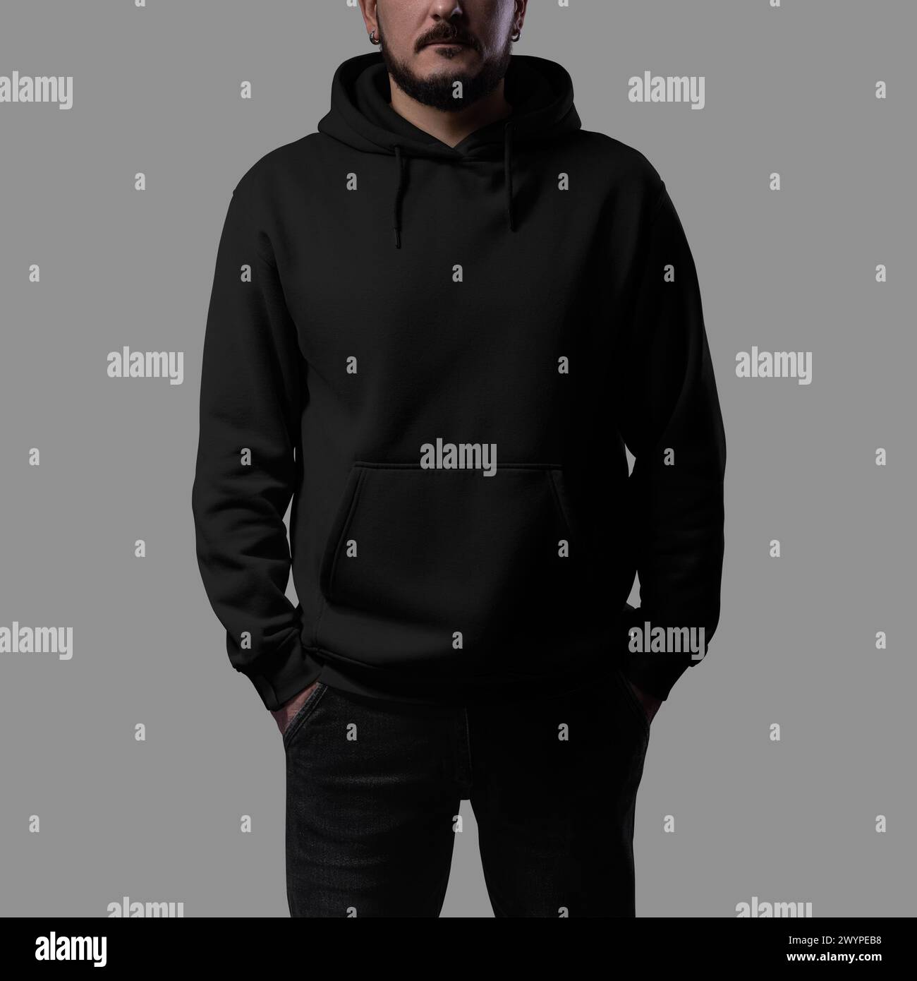 Template of a black oversized hoodie on a brutal man with his hands in pockets, wide clothing for design, branding, advertising, front view. Casual ap Stock Photo