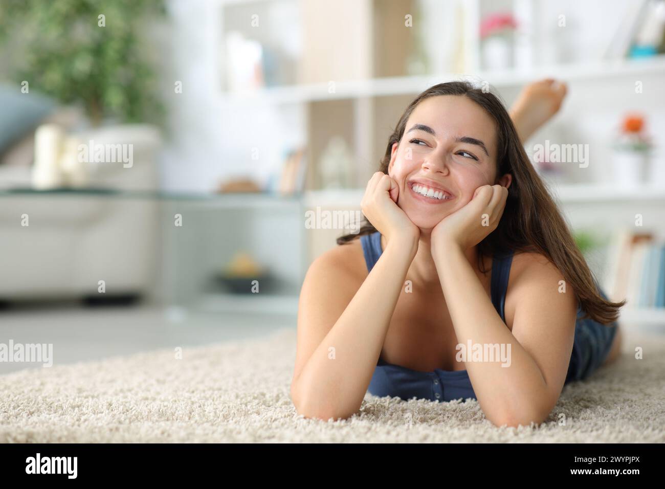 Happy woman dreaming looking above lying on a carpet at home Stock Photo