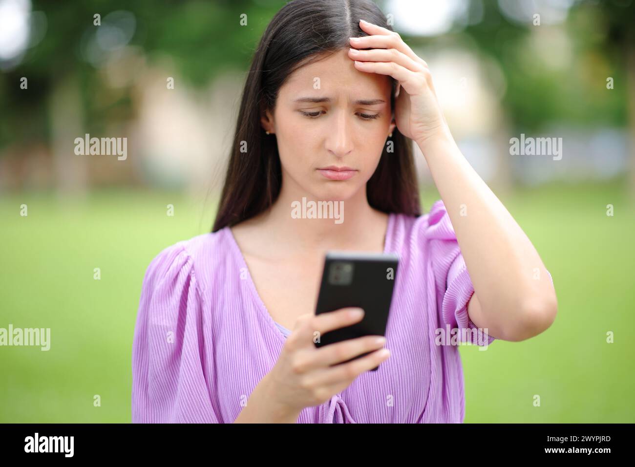 Front view portrait of a worried woman checking bad news on smart phone in a park Stock Photo