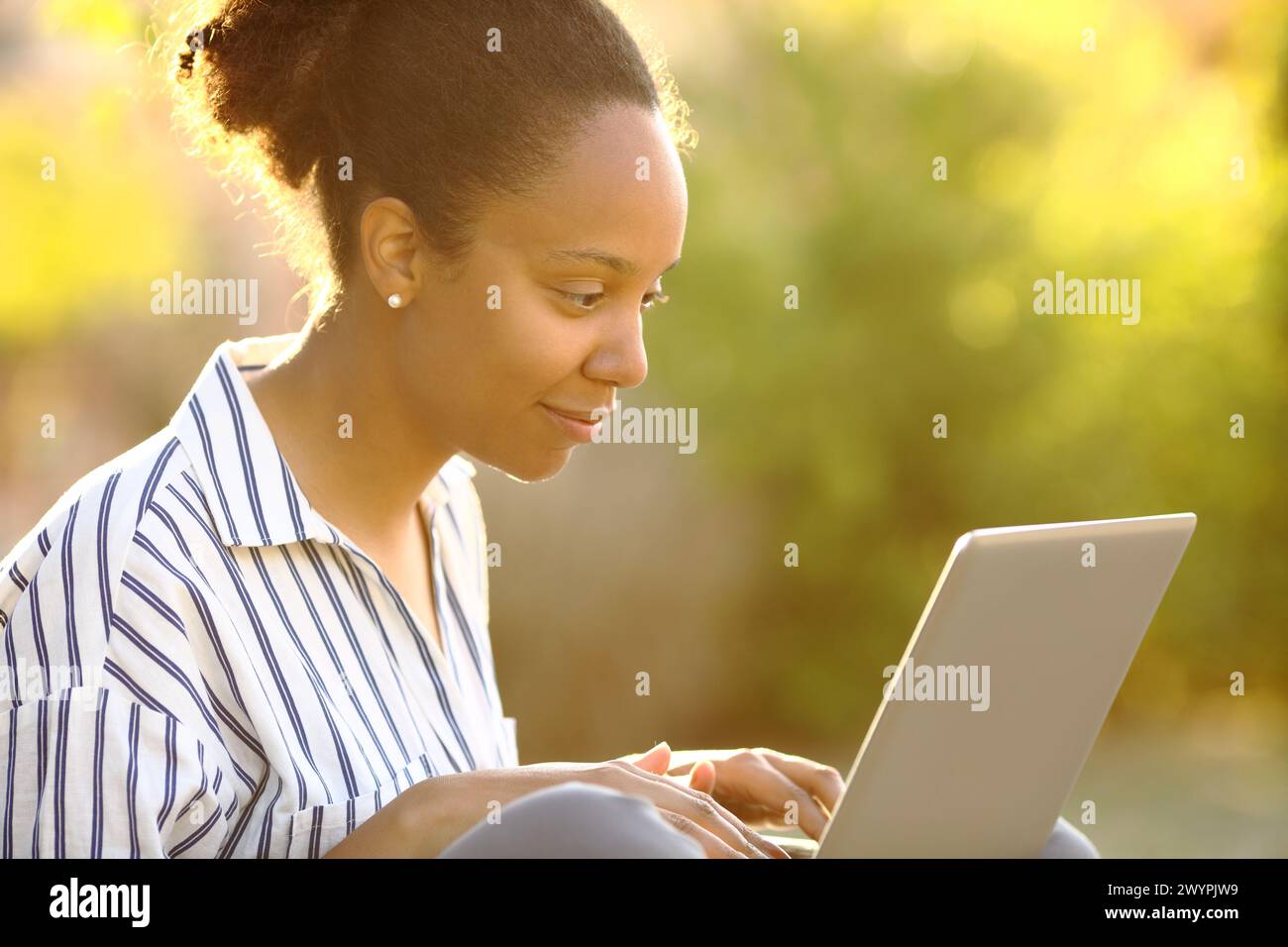 Black woman in a garden using laptop at sunset Stock Photo
