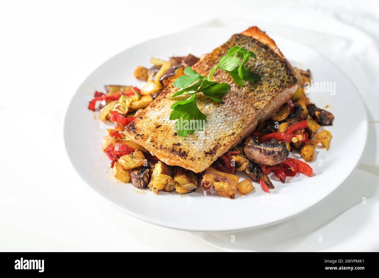 Rain trout fillet with a crispy fried skin on vegetables from the oven and parsley garnish served on a white plate, healthy fish dish suitable for low Stock Photo
