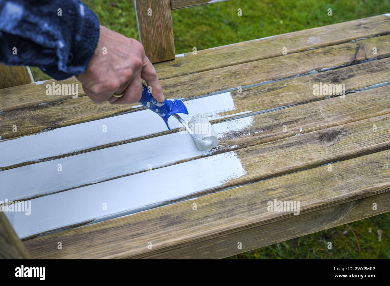 Man is painting a weathered wooden outdoor bench with a white weather