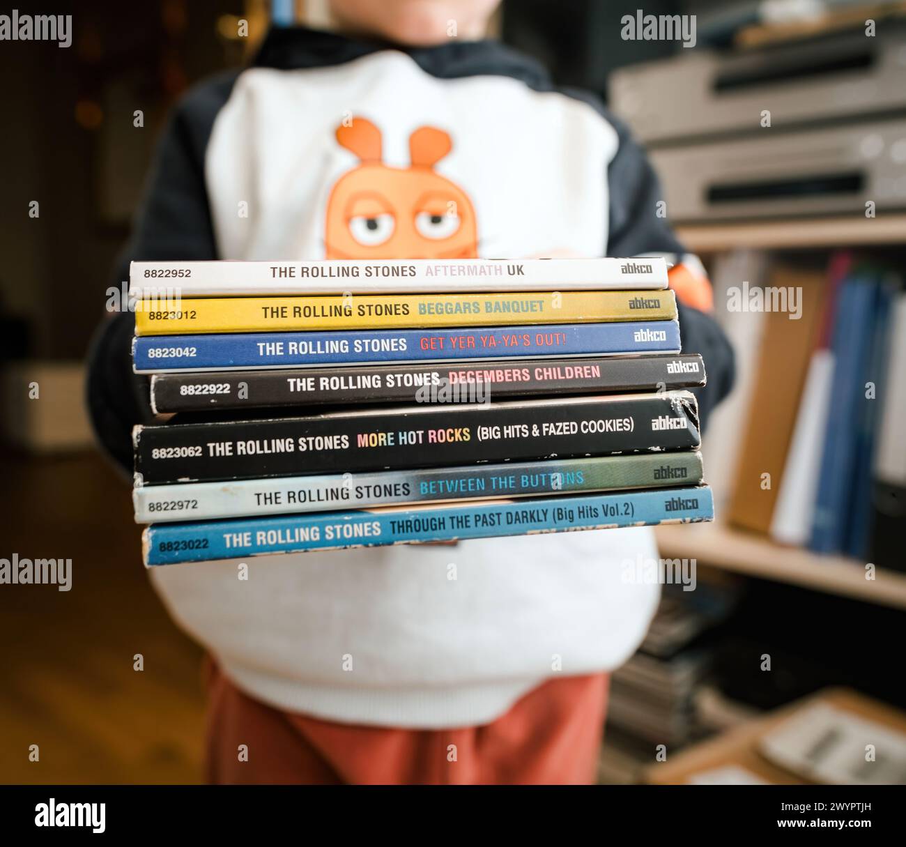 Frankfurt, Germany - Jan 12, 2024: A small child holds a stack of The Rolling Stones albums, partially obscuring their face, in a charming display of early music appreciation. Stock Photo
