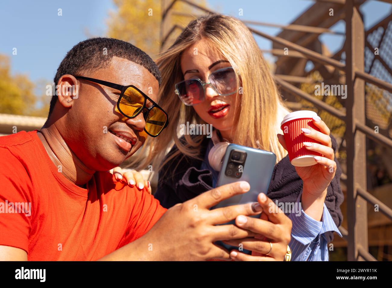 Happy interracial couple checking cell phone outdoors. Stock Photo