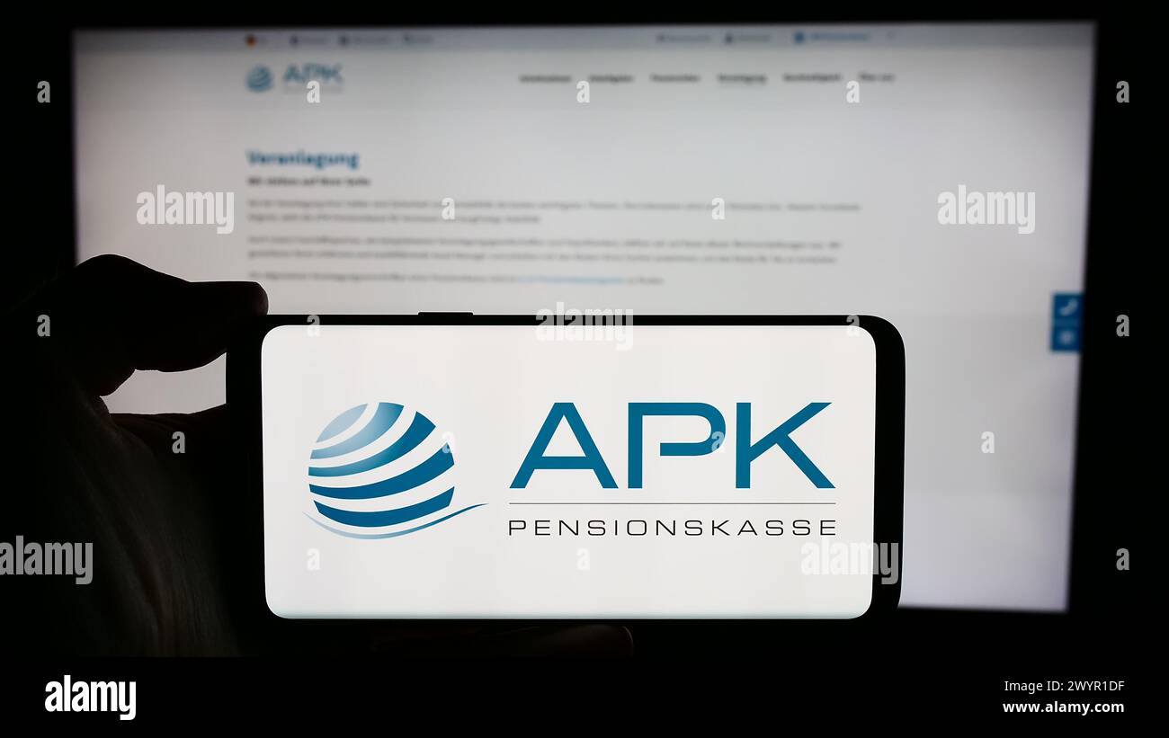 Person holding cellphone with logo of pension scheme institution APK Pensionskasse AG in front of webpage. Focus on phone display. Stock Photo