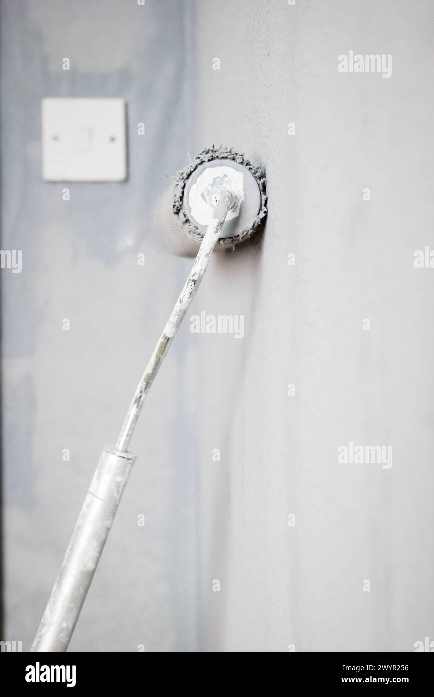 Paint roller extendable pole over painted woodchip wallpaper wall