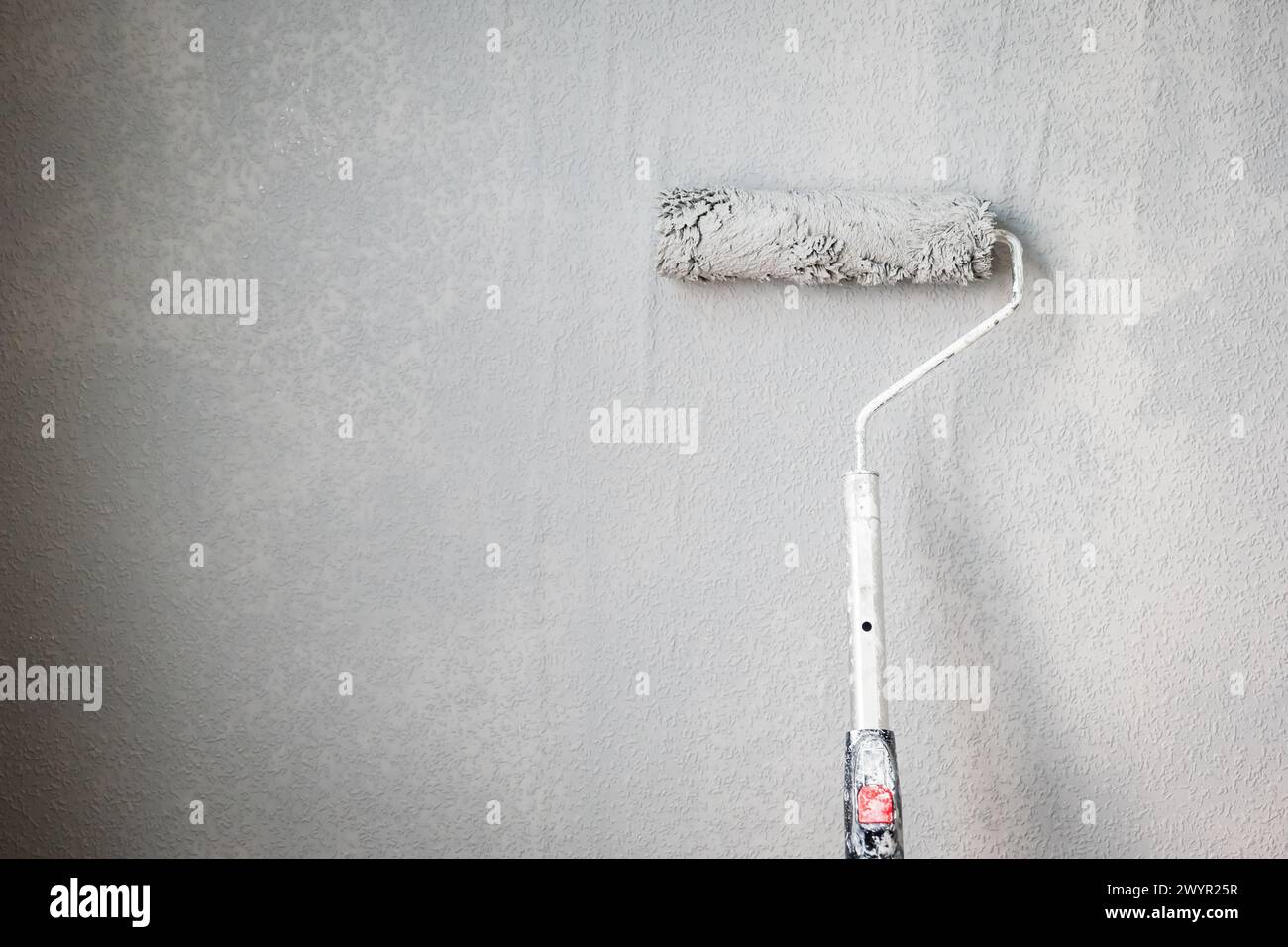 Paint roller extendable pole over painted woodchip wallpaper wall