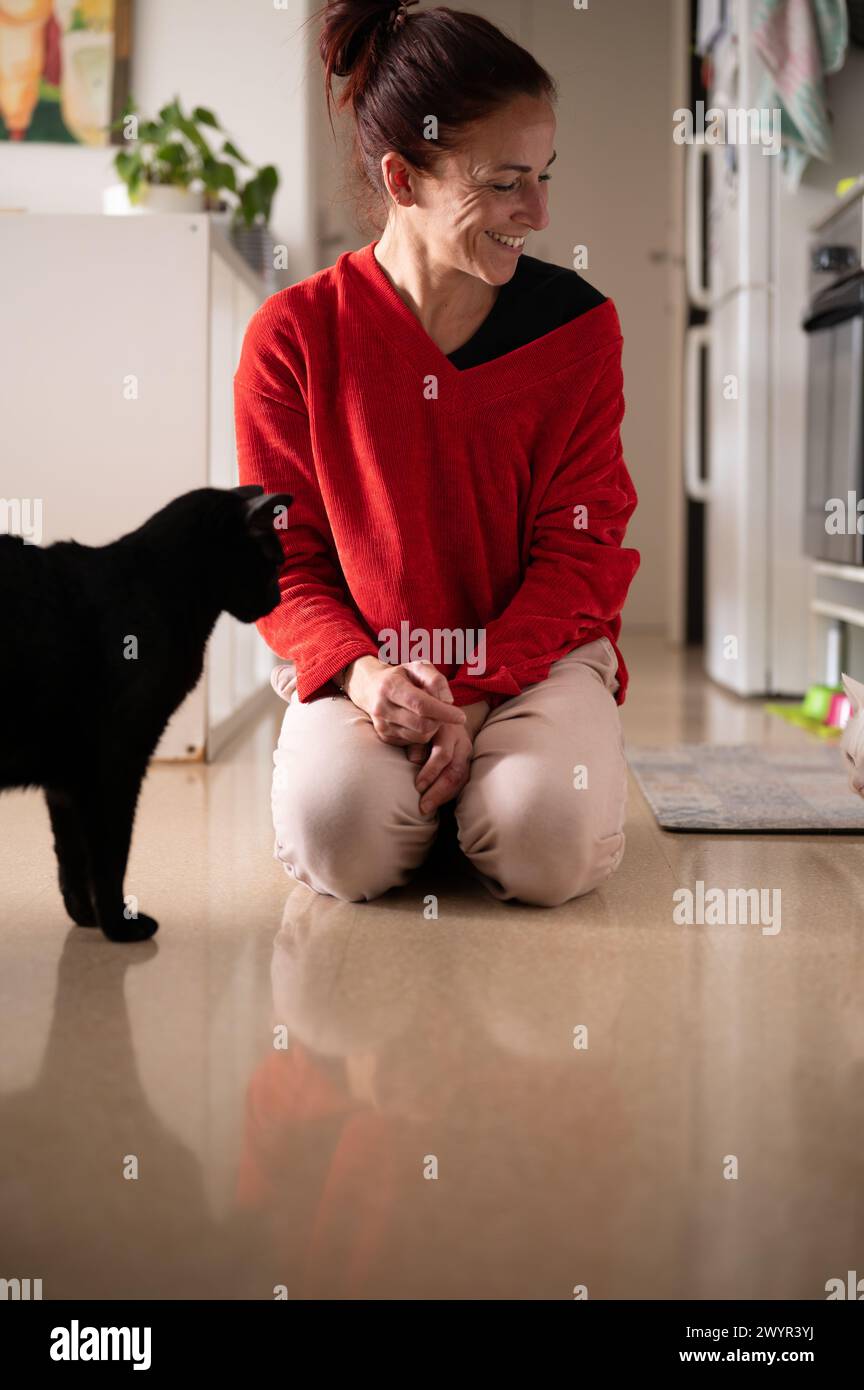 Cheerful lady kneeling on floor near domestic cat Stock Photo