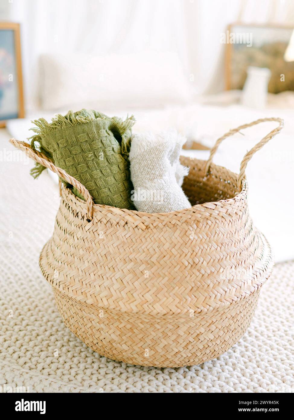 Light wicker basket with rolled blankets in a neutral space Stock Photo