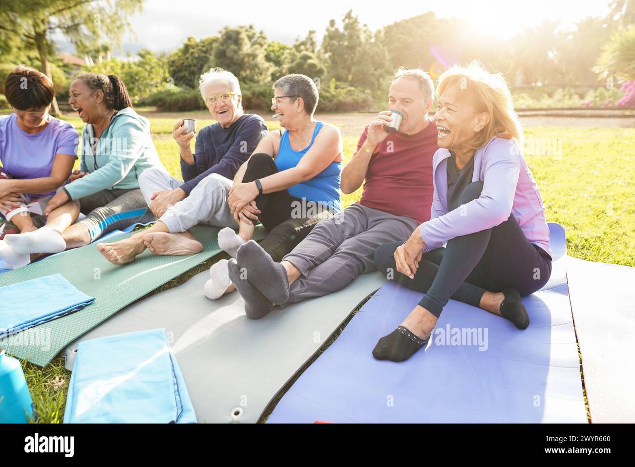Senior people having fun after yoga session chatting and drinking hot tea at city park - Mature friends laughing together after sport routine Stock Photo