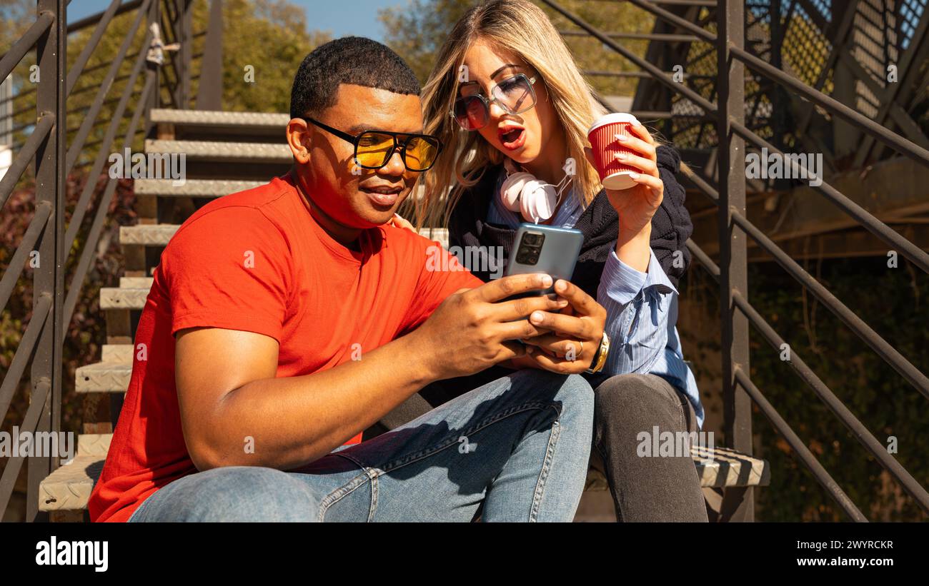 Happy interracial couple checking cell phone outdoors. Stock Photo