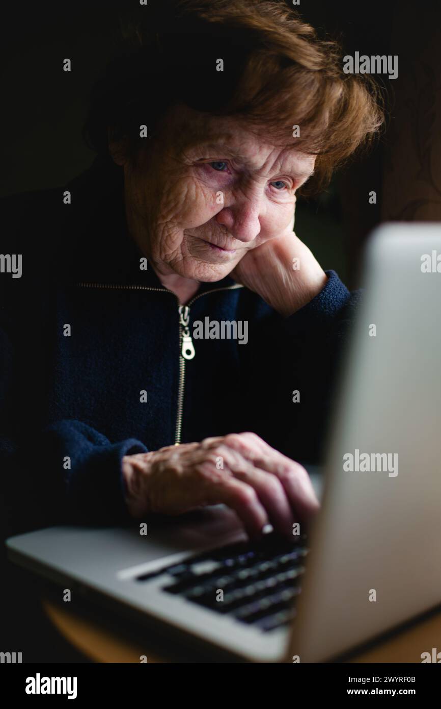 An old woman sits with her laptop. Stock Photo