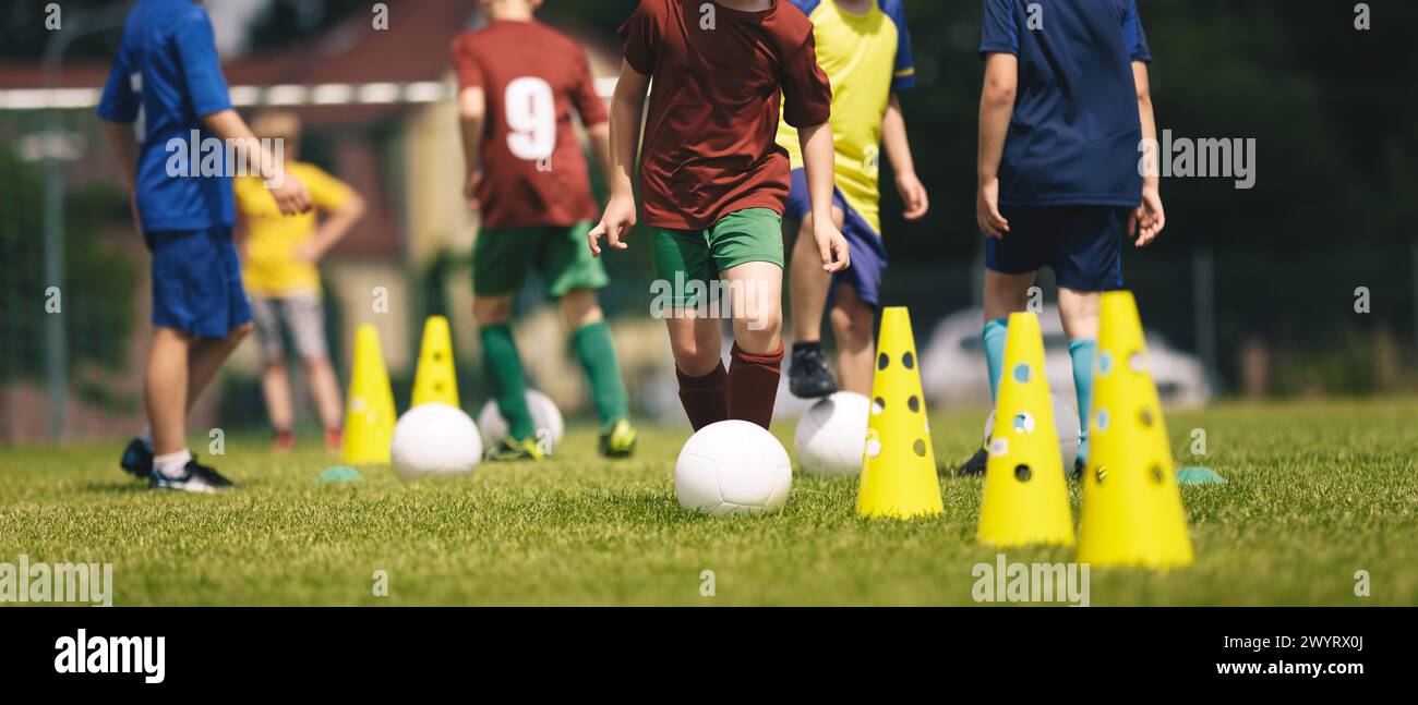 Slalom practice for football players. Youth in sports training. Player kicking ball during a soccer training drill. Summer sports practice camp for sc Stock Photo
