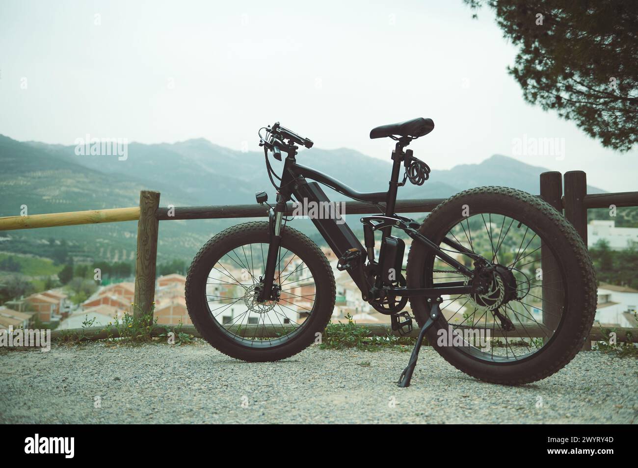 A modern black electric bike on the countryside road, parked by a wooden fence, against mountains background in the nature. Copy advertising space. En Stock Photo