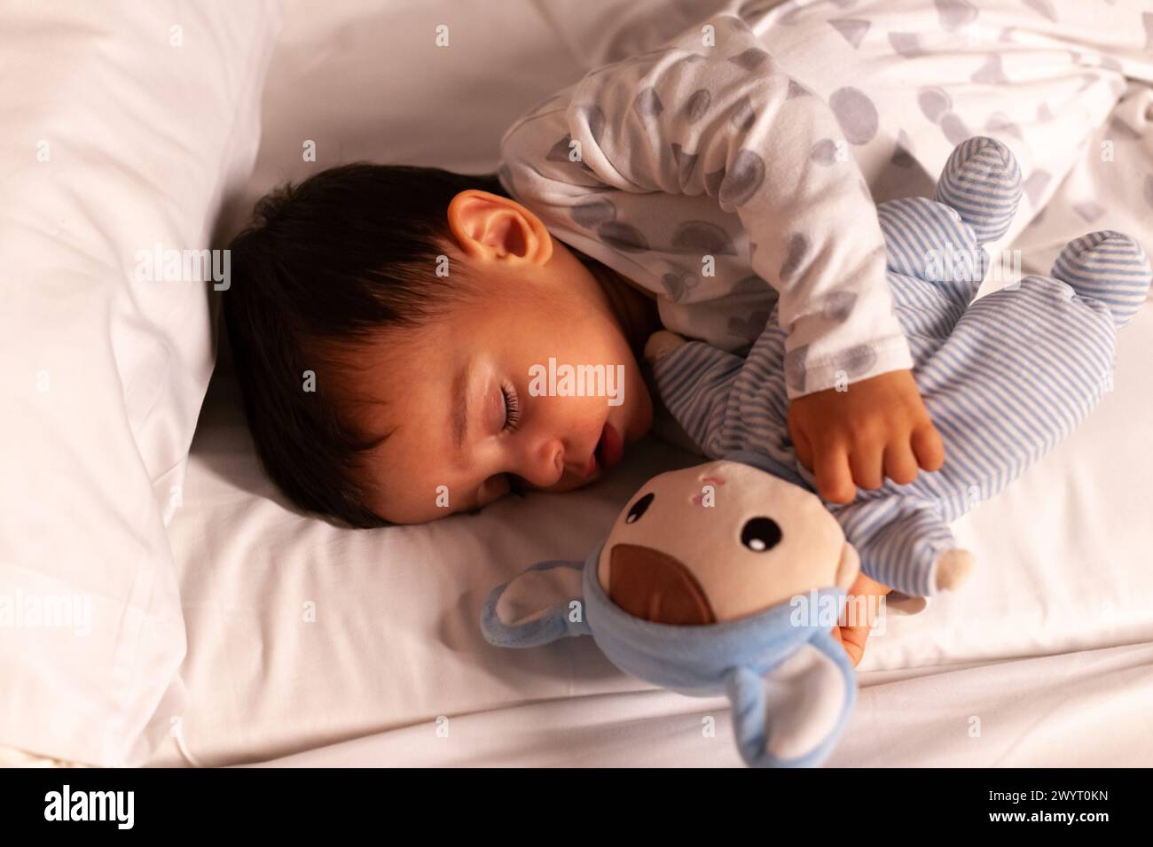 Baby sleeping with mouth open and cuddling teddy bear in bed Stock Photo