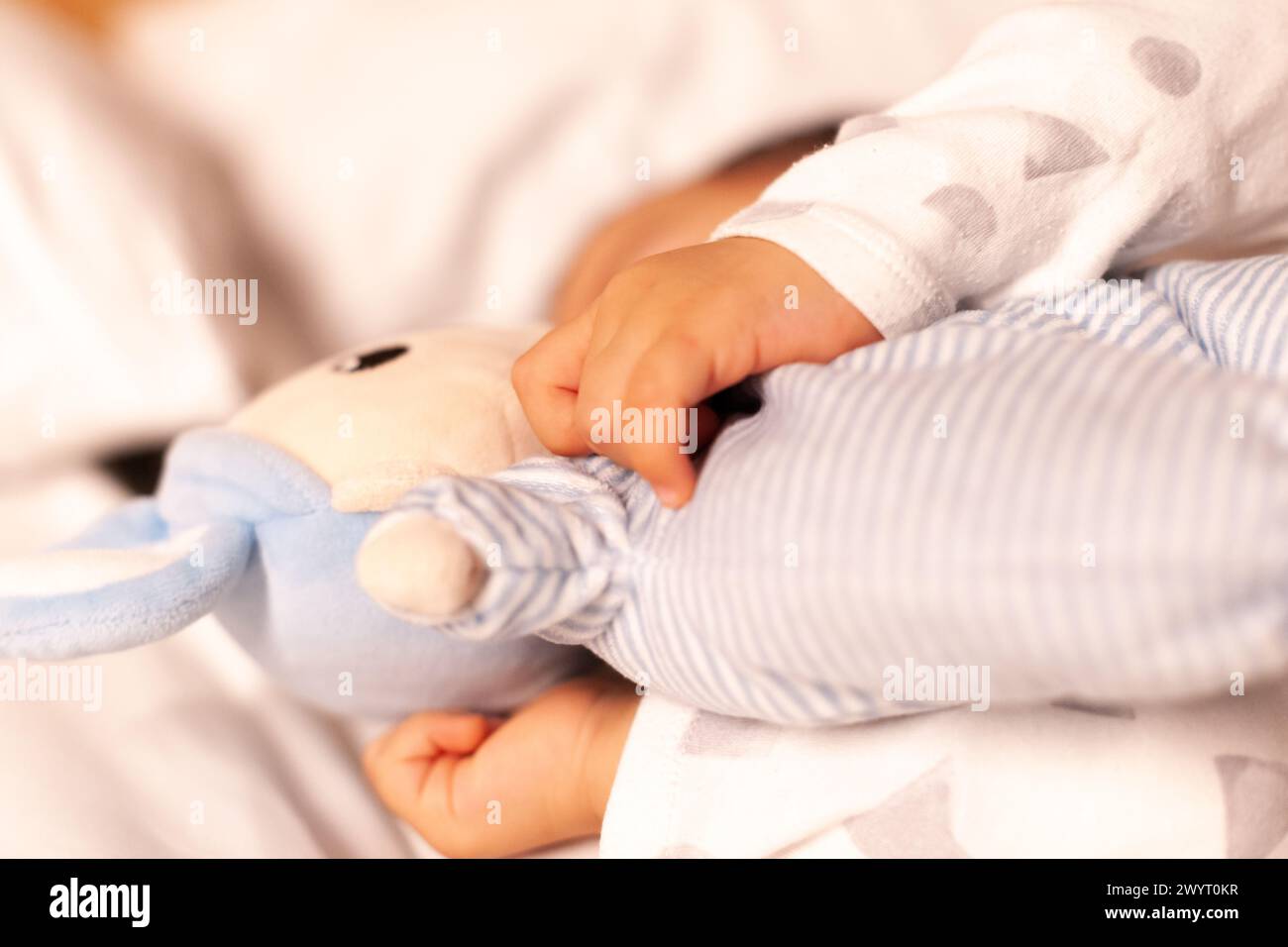 baby's hands holding doll while sleeping Stock Photo