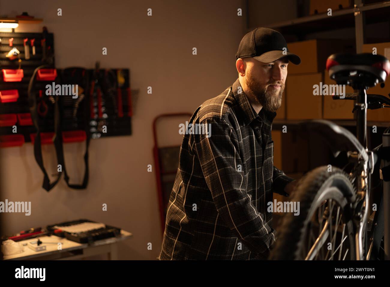 Handsome bearded mechanic repairing bicycles in a workshop or garage. Stock Photo