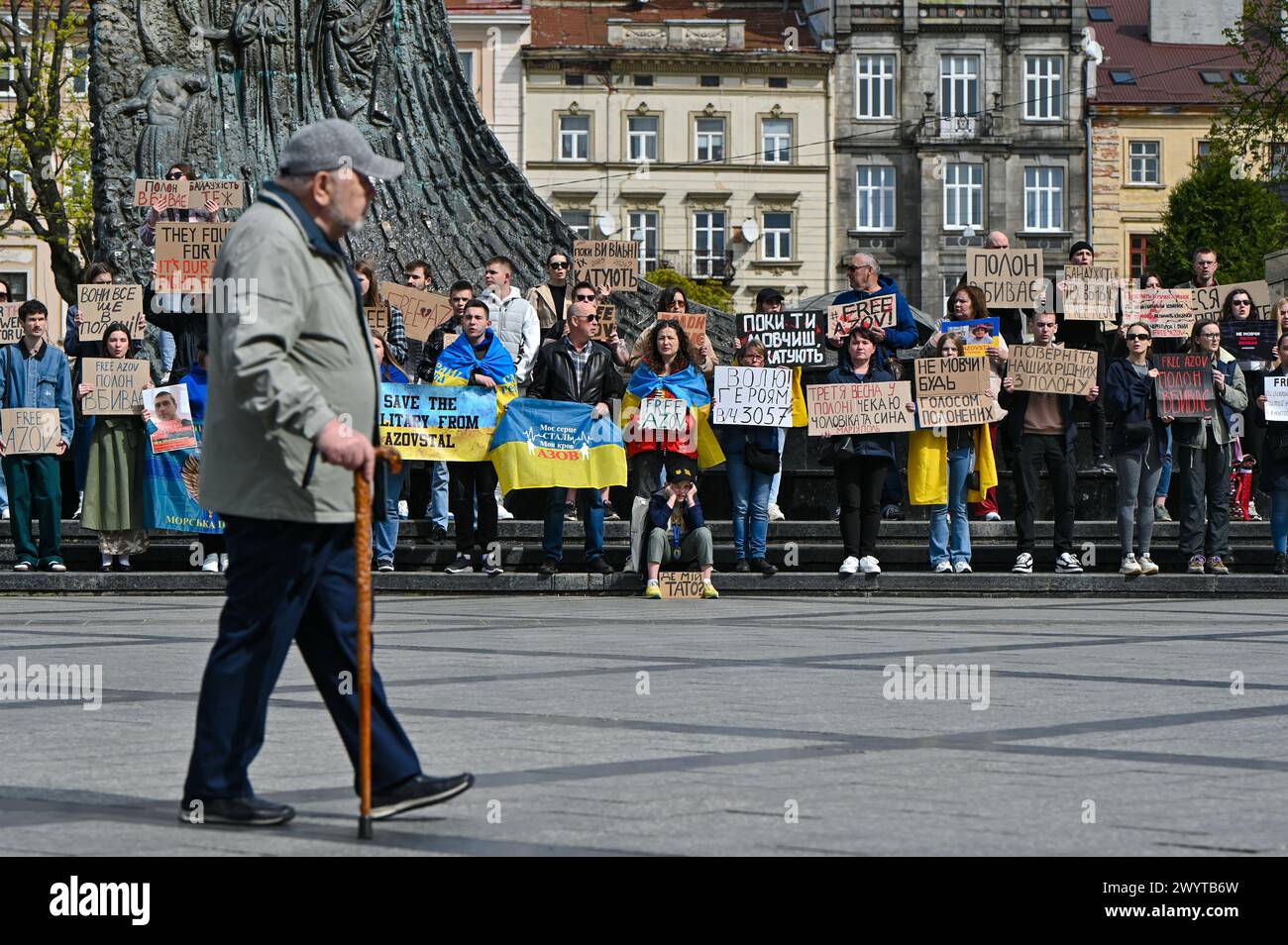 LVIV, UKRAINE - APRIL 6, 2024 - A senior man with a cane walks past demonstrators holding placards in the square at the Taras Shevchenko monument during a rally held as part of the Don’t Be Silent! Captivity Kills! initiative to remind about Ukrainian military personnel kept in Russian captivity and those who went missing, Lviv, western Ukraine. Stock Photo