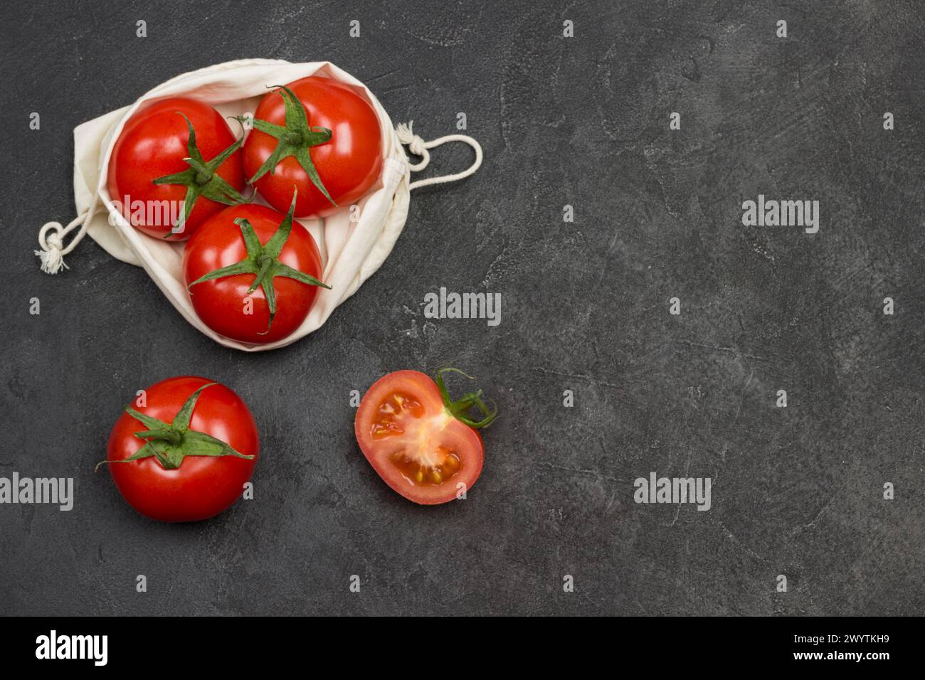 Tomatoes in  reusable mesh bag. Whole tomato and chopped tomato wedges on table. Black background. Top view. Copy space Stock Photo