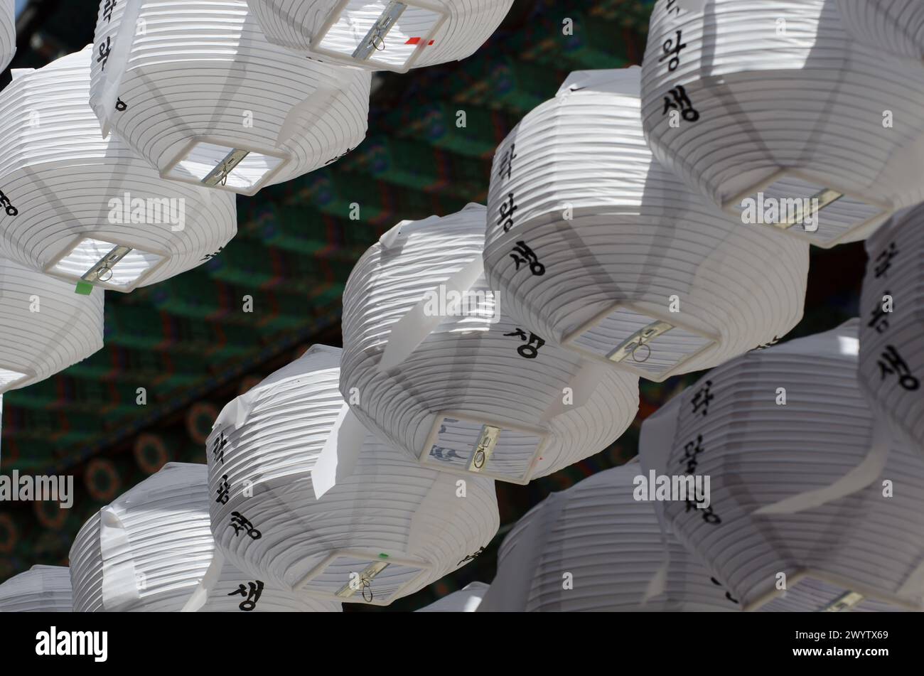 A row of lanterns with Chinese writing on them. The lanterns are white and are hanging from a building Stock Photo