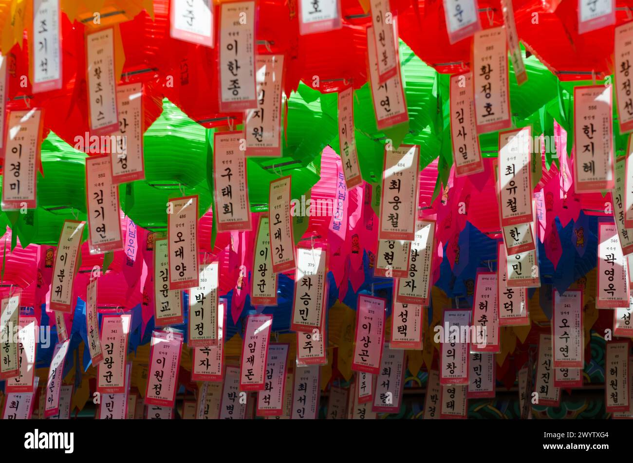 A colorful display of lanterns with Chinese writing on them. The lanterns are hanging from the ceiling and are of various colors Stock Photo