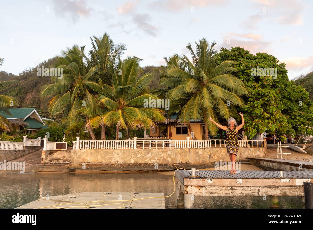 A woman stands on a dock off the lagoon that surrounds the lush South Pacific island of Mo'orea, French Polynesia. Stock Photo