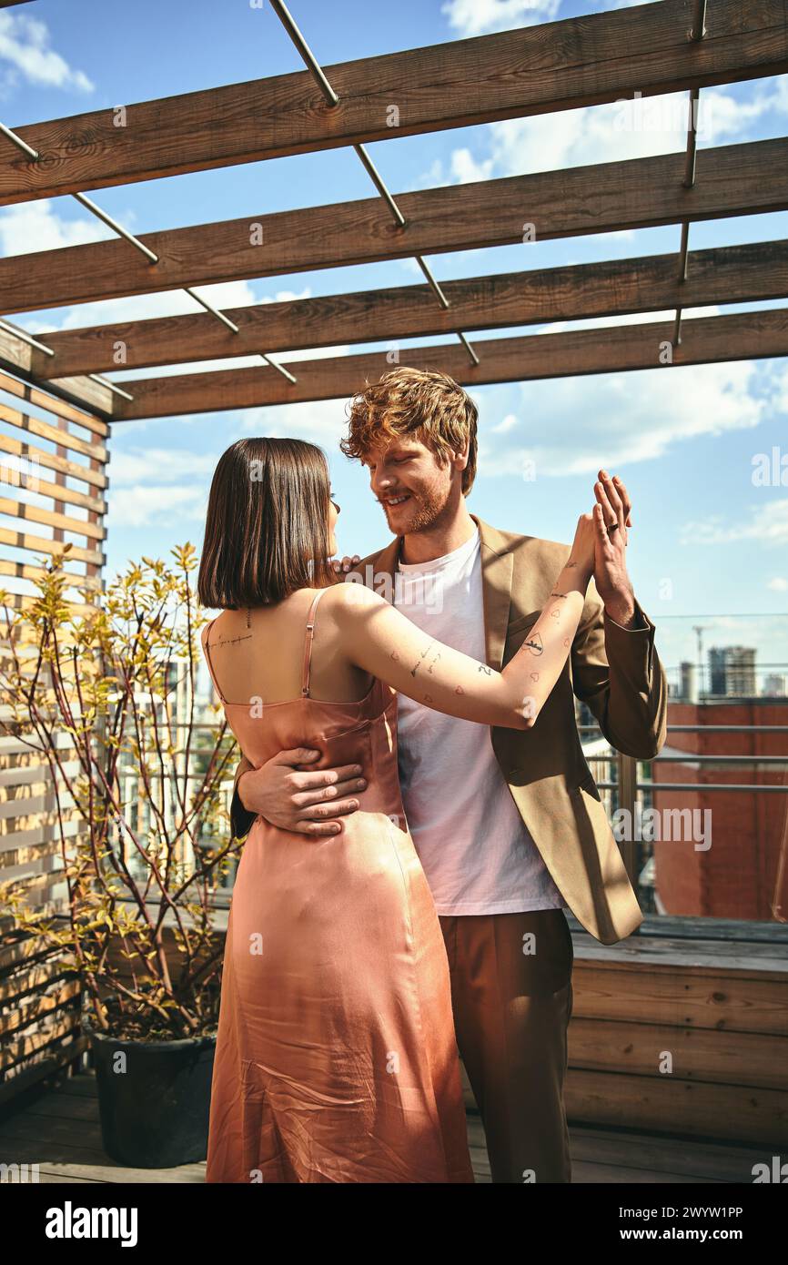 A man and woman stand on top of a rooftop, gazing at the view below ...