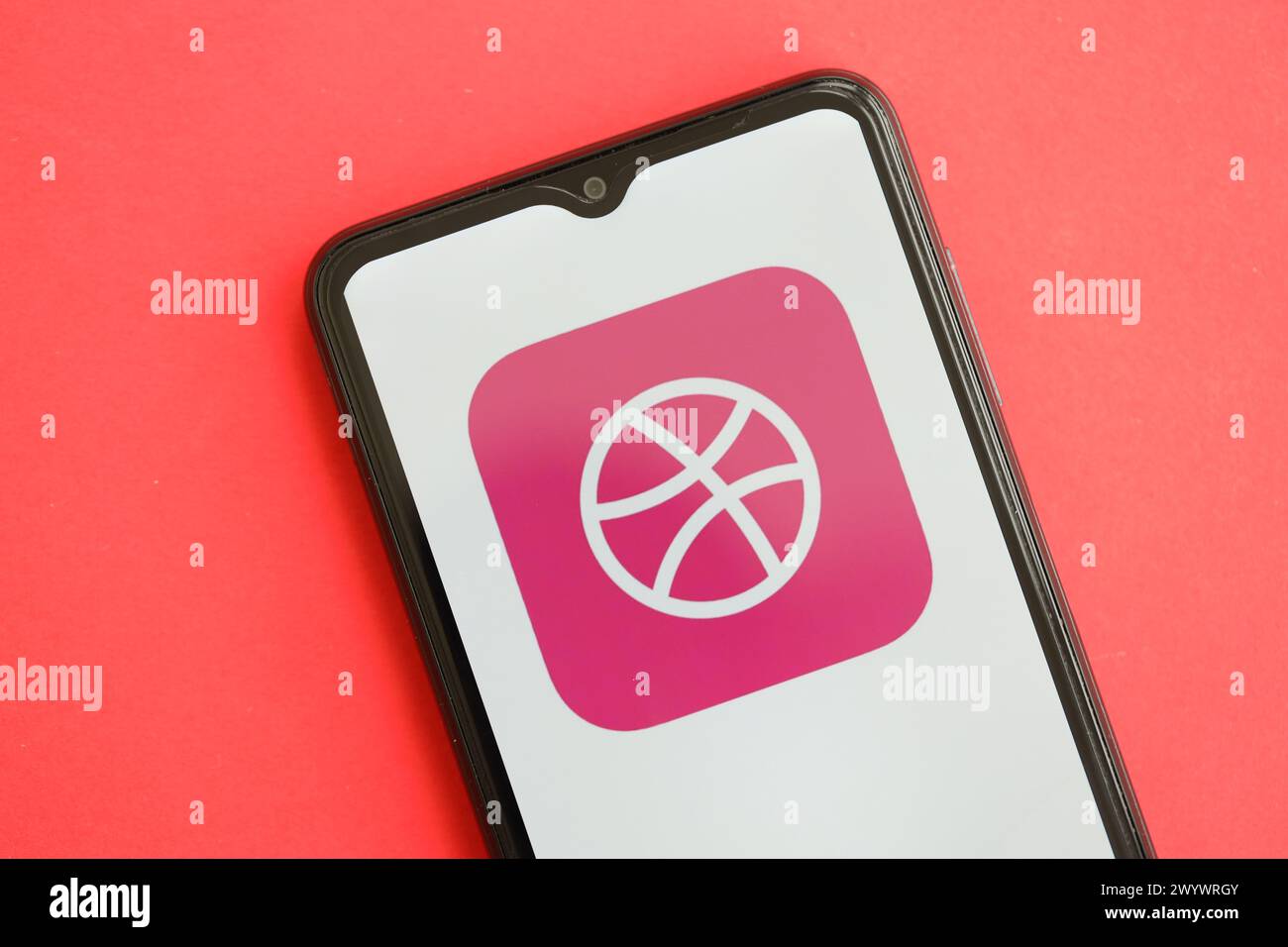 KYIV, UKRAINE - APRIL 1, 2024 Dribbble icon on smartphone screen on red table close up. iPhone display with app logo on bright red background Stock Photo