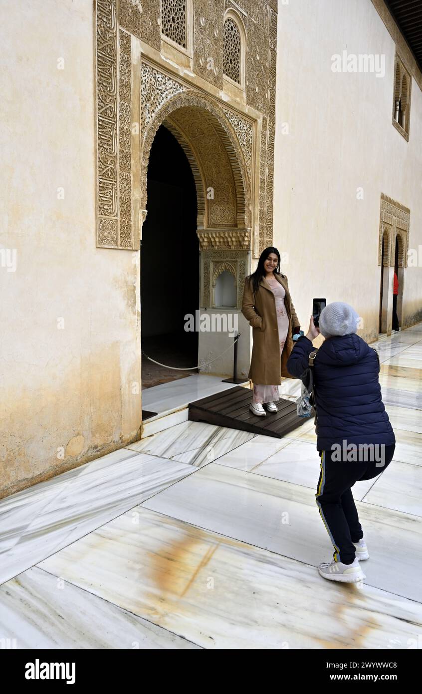 Tourist taking photograph of friend by elaborate Moorish-style archway  inside Nasrid Palaces, Alhambra Palace, Granada, Spain Stock Photo