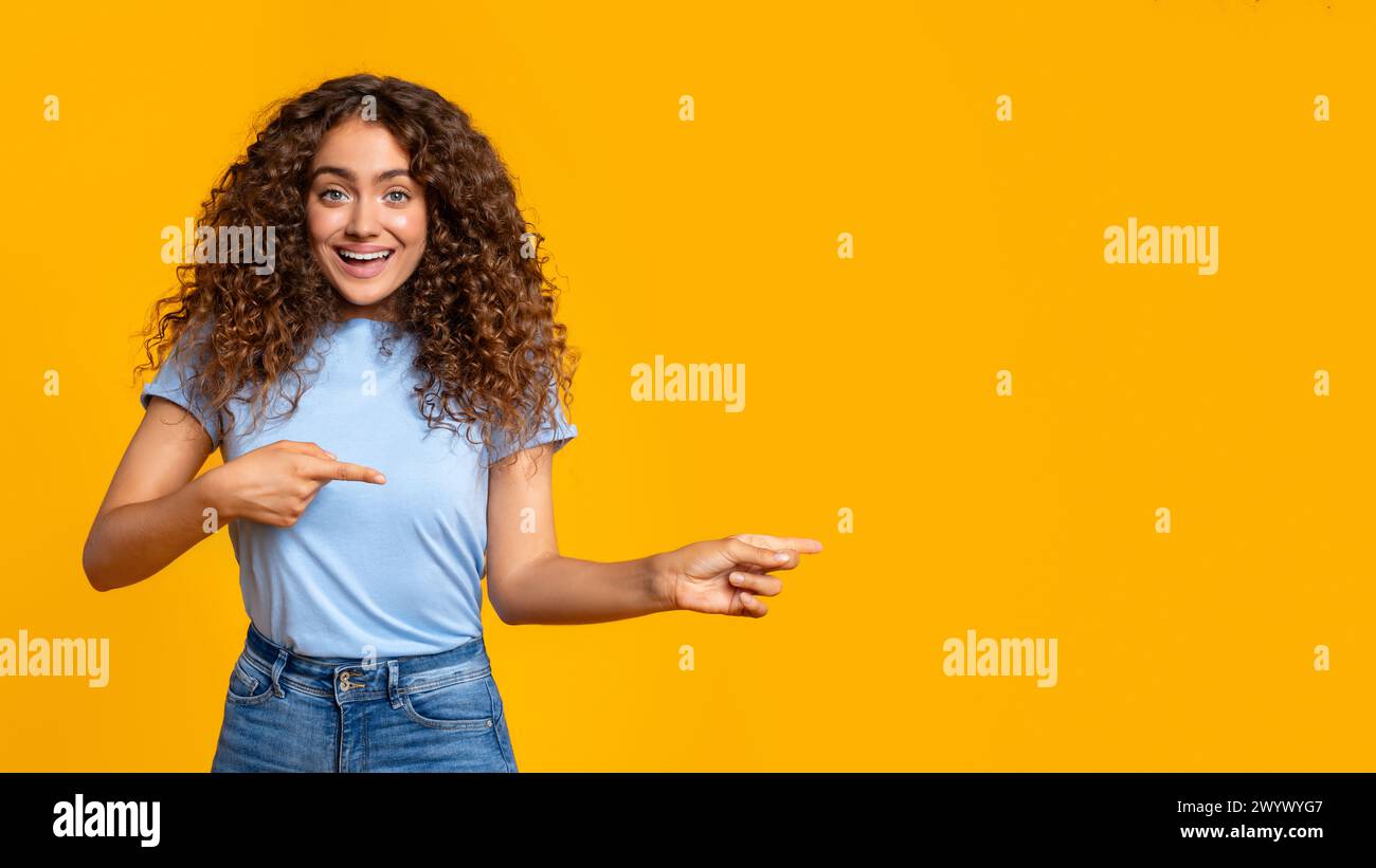 Woman pointing and looking surprised on yellow Stock Photo
